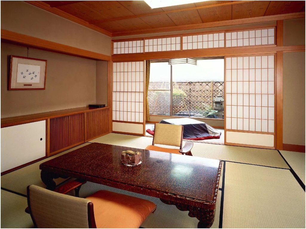 Traditional Japanese ryokan featuring elegant tatami room with low wooden table, silk cushions, and ornate sliding doors opening to garden view