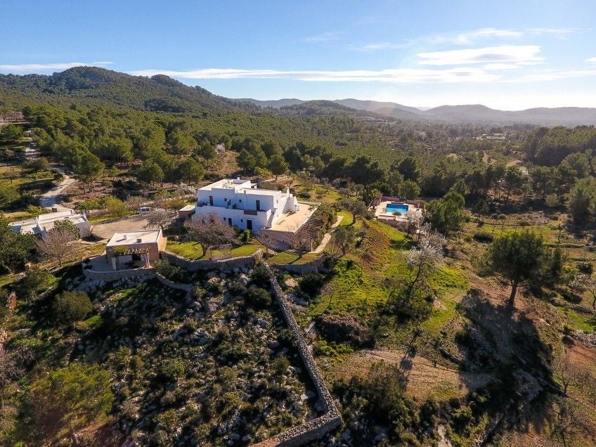 Traditional Spanish stone villa with rustic wooden shutters, surrounded by lush Mediterranean gardens and a serene infinity pool at sunset