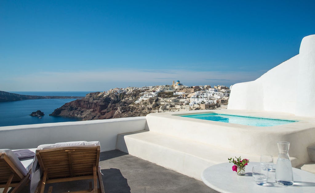 Elegant whitewashed luxury cave hotel in Santorini with infinity pool overlooking the Aegean Sea, framed by curved blue-domed archways