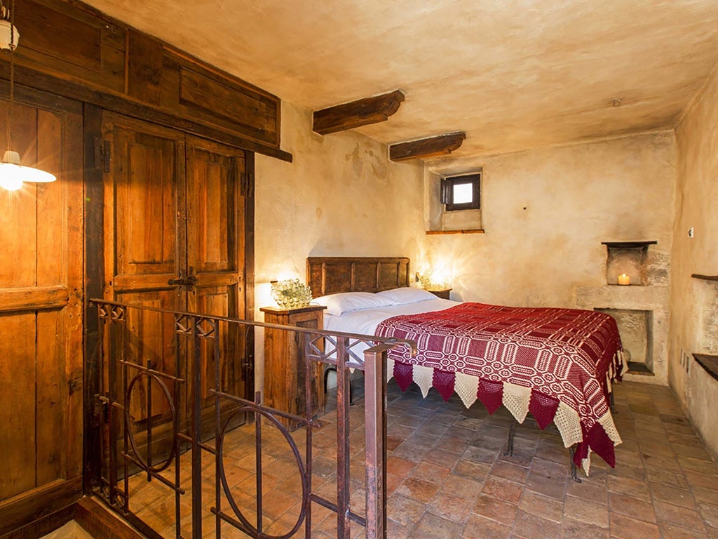 Rustic stone-walled bedroom with antique wooden bed, soft linens, and warm candlelight in historic Italian mountain hotel suite