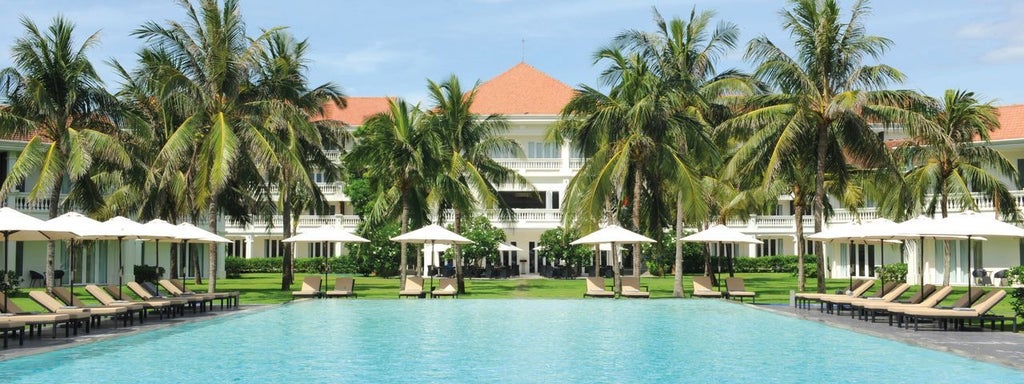 Elegant white colonial-style resort with traditional Vietnam architecture, palm trees and manicured gardens along Thu Bon riverside