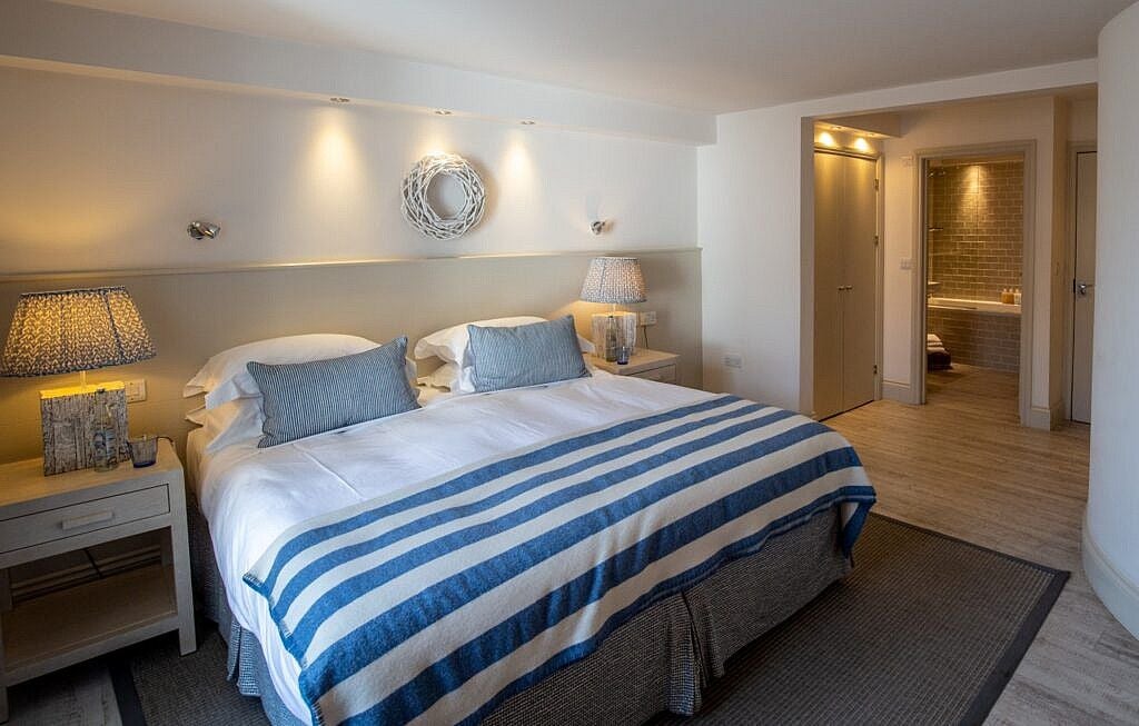 Elegant coastal village room at scenset hotel, featuring crisp white linens, nautical accents, and panoramic views of UK seaside landscape through large windows.