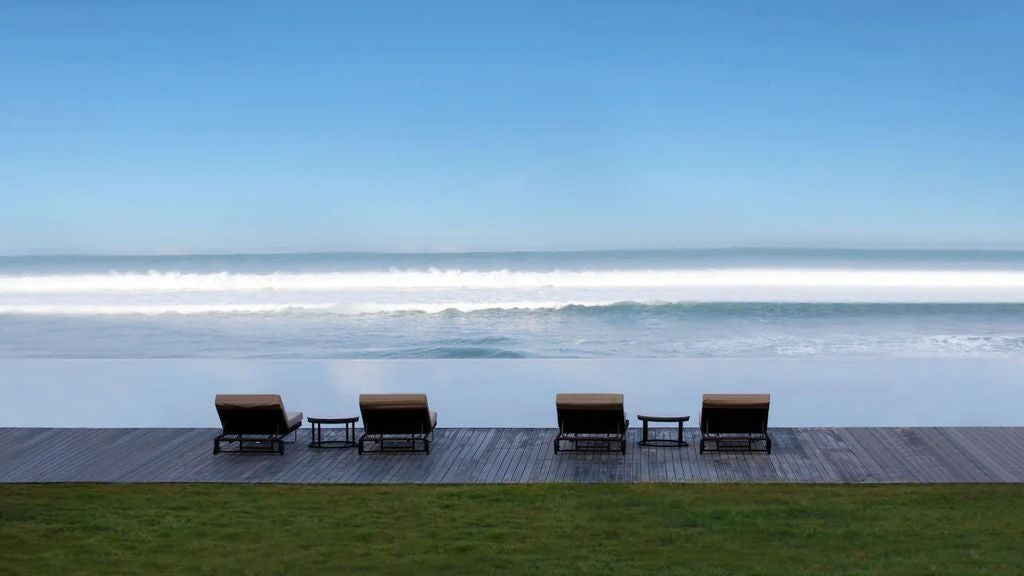 Modern beachfront hotel with infinity pool overlooking Seminyak Beach, featuring contemporary architecture and swaying palm trees