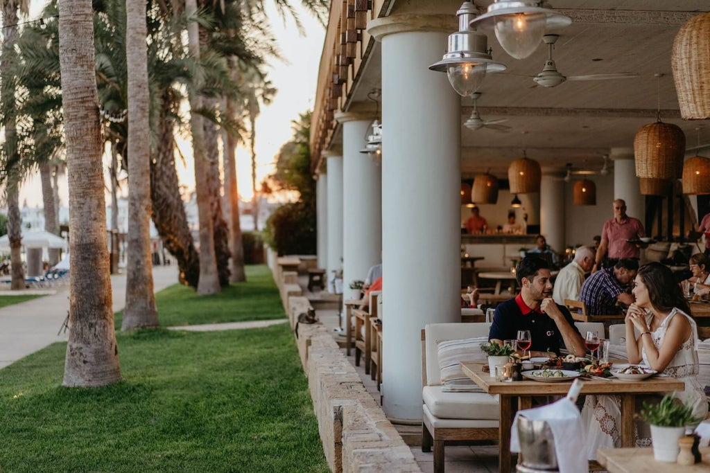 Luxurious beachfront scenset hotel with crystal-clear blue waters, white sandy beach, and elegant Mediterranean-style architecture gleaming under bright sunlight