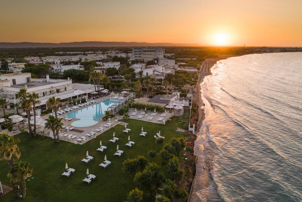 Luxurious white-walled Mediterranean hotel with sleek pool, sun loungers, and lush greenery against a pristine coastal backdrop in Southern Italy