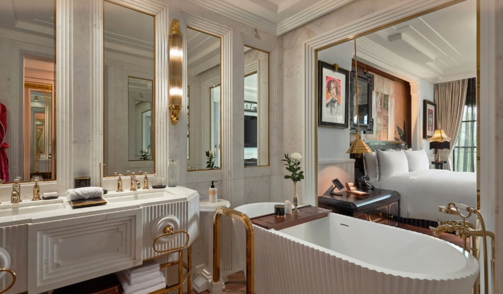 Elegant Deluxe Suite with plush king bed, Art Deco-inspired decor, crystal chandelier and floor-to-ceiling windows overlooking Hanoi's skyline