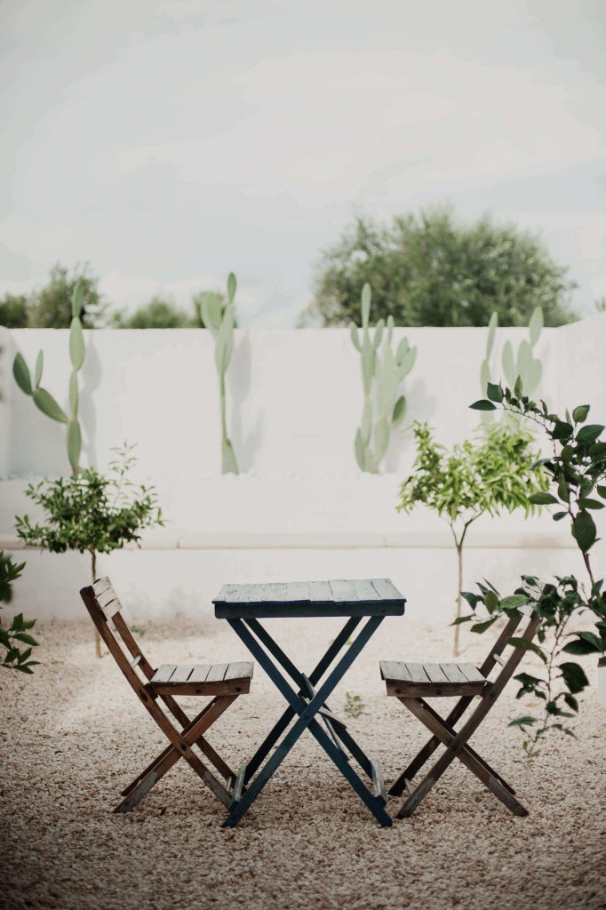 Minimalist white stone farmhouse surrounded by olive groves, showcasing rustic elegance against golden Puglia landscape with Mediterranean sunlight