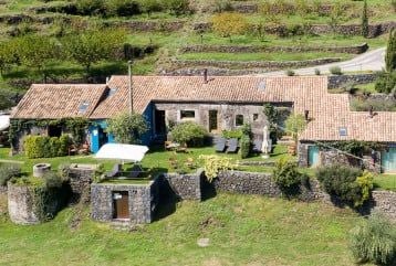 Elegant Sicilian estate suite with rustic stone walls, minimalist decor, plush white bedding, and panoramic views of Mount Etna's volcanic landscape