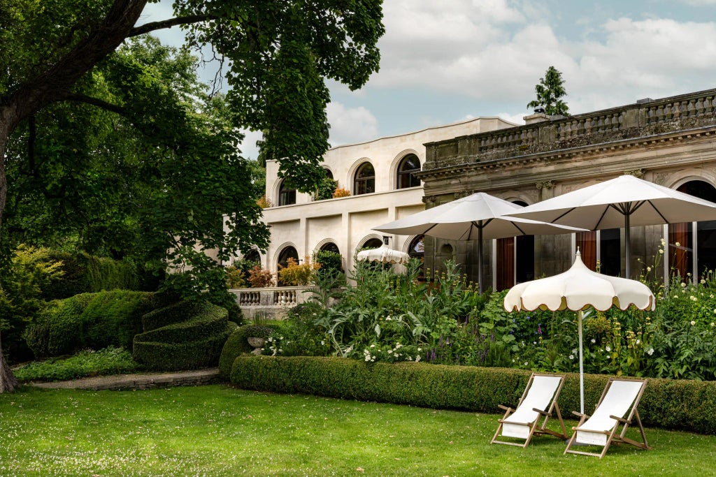 Luxurious stone country house hotel with modern glass extension, nestled in lush green countryside near scenic Cotswolds landscape