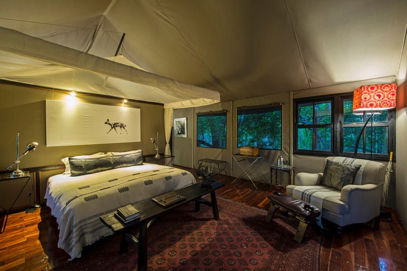 Elevated wooden deck and luxury safari tent with plush seating overlooks tranquil wetlands during golden Botswana sunset