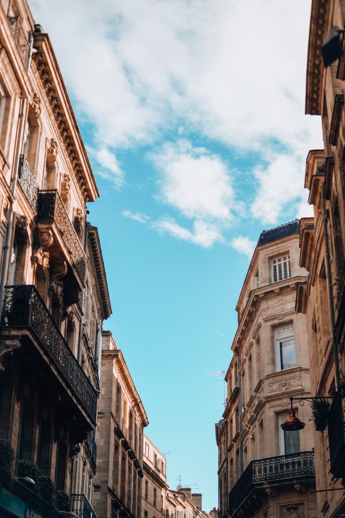 Elegant townhouse facades with ornate balconies line historic cobblestone street in Bordeaux, bathed in warm golden sunlight at sunset