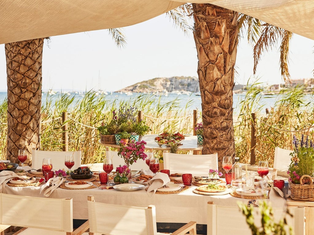 Luxurious beachfront suite at a high-end resort with white-draped four-poster bed, turquoise ocean view, and modern minimalist design in Ibiza