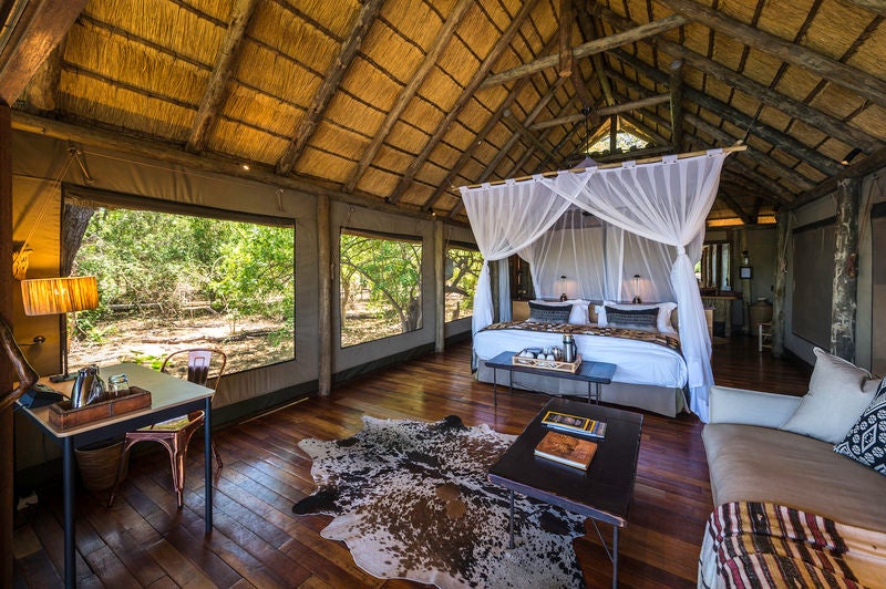 Elevated luxury safari suite with private deck overlooking African savanna, featuring elegant wood and canvas design at sunset