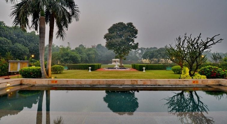 Ornate colonial-style luxury hotel with white facade, manicured gardens, grand pillars and palm trees against blue Indian sky