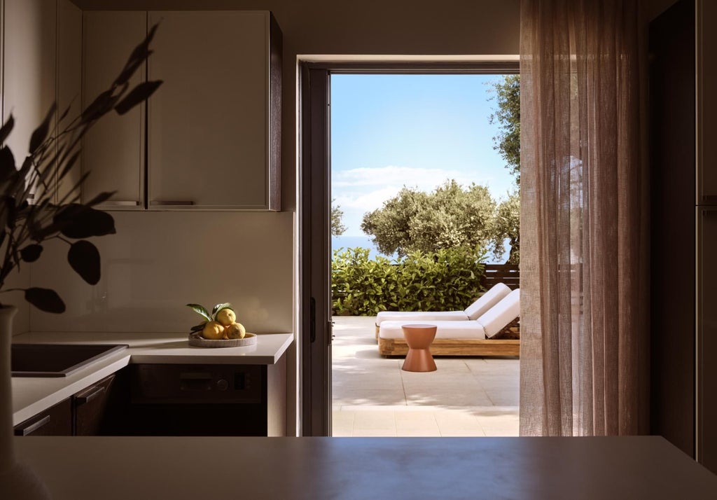 Elegant Mediterranean villa bedroom with white-draped king bed, stone walls, wooden floors, and panoramic Aegean Sea view through arched window