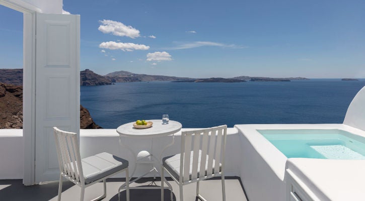 Luxurious white-washed suites with private infinity pools overlooking Santorini's caldera and Aegean Sea during golden sunset