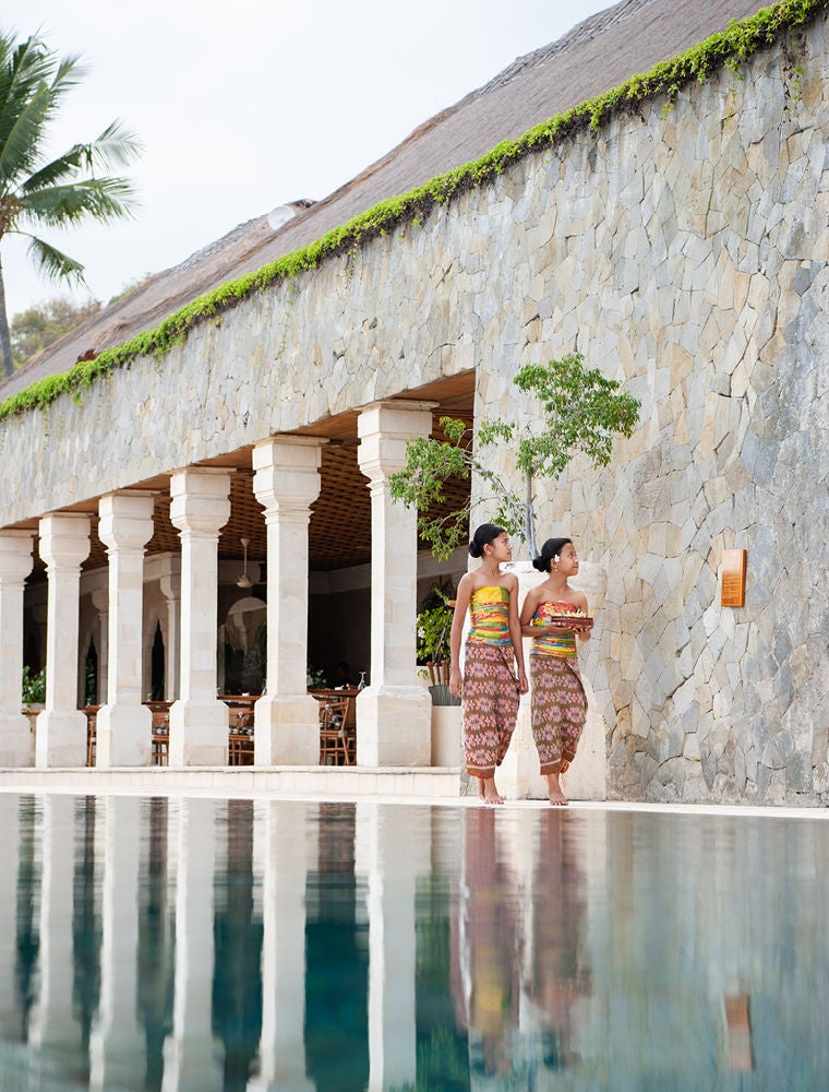 Three-tiered infinity pools cascading down a lush hillside, overlooking the Bali Sea with Mount Agung volcano in the hazy distance