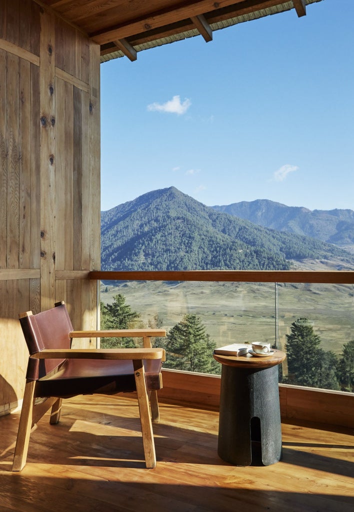 Luxurious mountain lodge with floor-to-ceiling windows overlooking Bhutanese valley, featuring timber architecture and private terrace