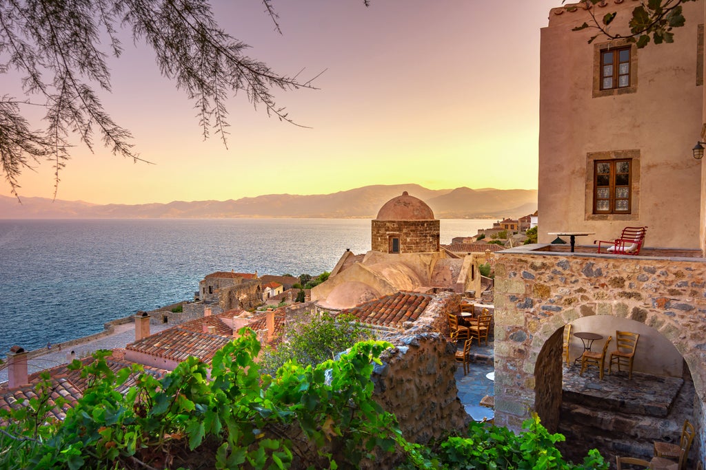 Medieval stone fortress of Monemvasia perched on rocky island, golden sunset light illuminating Byzantine walls and azure Aegean Sea backdrop