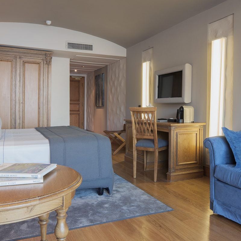 Elegant junior suite with sea-view balcony, featuring ornate baroque furnishings, white linens, and marble accents in warm sunlight