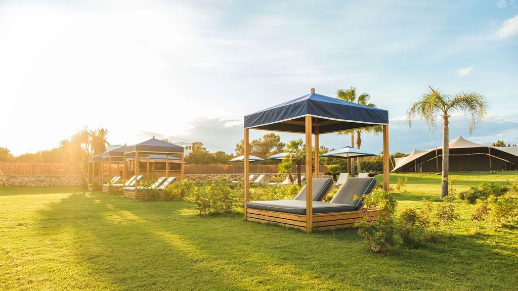 Luxurious beachfront hotel with white and blue Mediterranean design, palm trees, and infinity pool overlooking scenic Spanish coastline at sunset