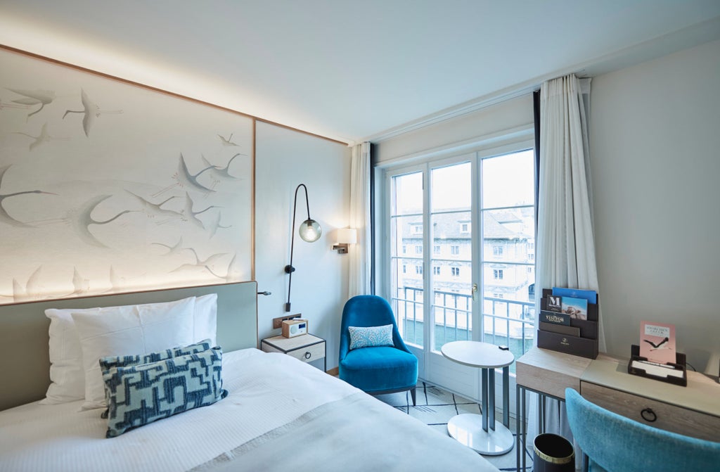 Elegant riverside queen room with floor-to-ceiling windows, plush white bedding, and modern Swiss decor overlooking the Limmat River views