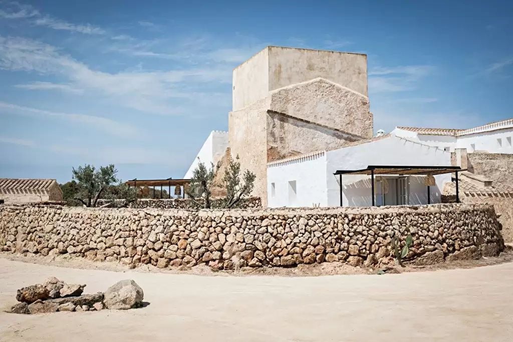 Elegant stone tower hotel in Menorca with rustic Mediterranean architecture, surrounded by manicured gardens and swaying palm trees