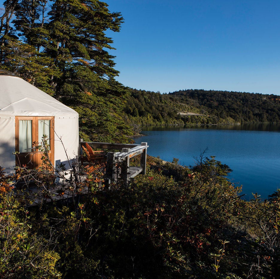 Geodesic dome luxury yurts nestled in Patagonian forest, with snow-capped mountains and pristine lake views in the background