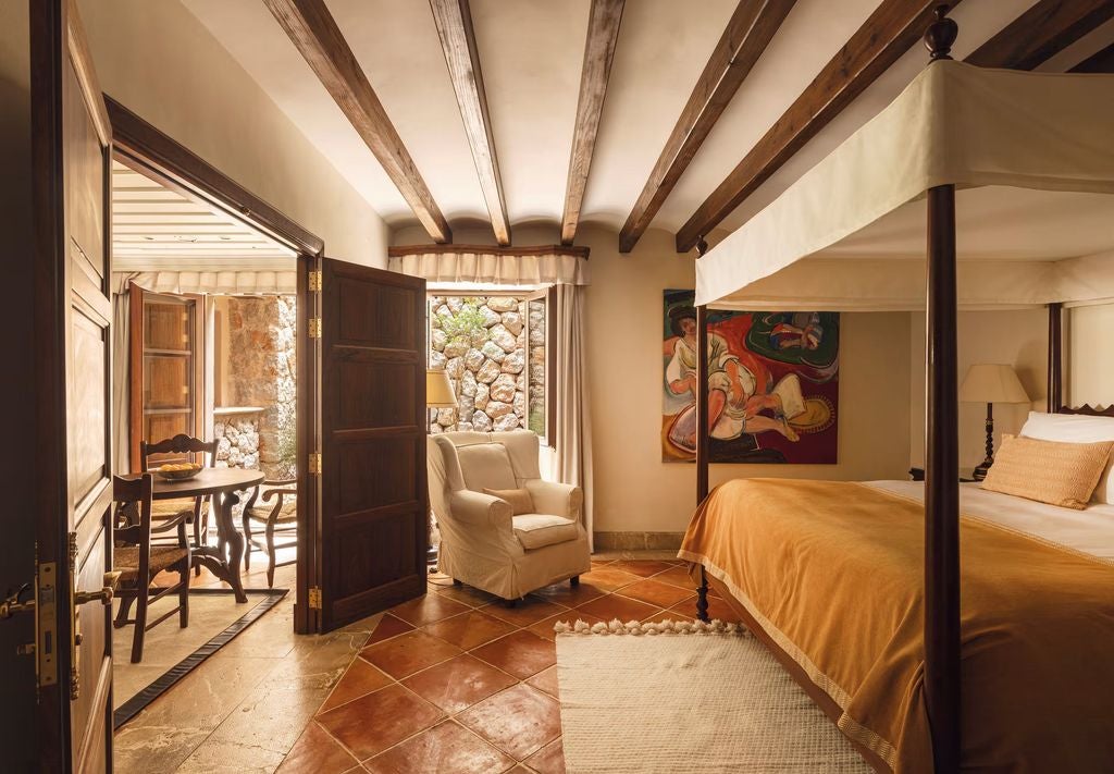 Elegant Mediterranean hotel suite with terracotta floors, white walls, exposed beams, and French doors opening to a private terrace.