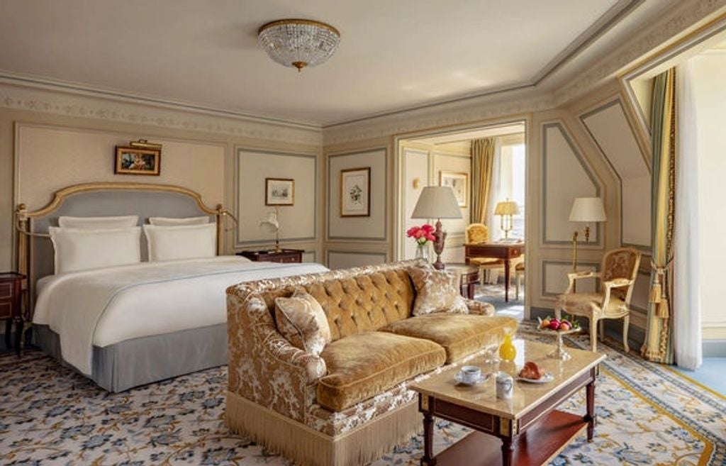 Opulent Junior Suite with crystal chandelier, gold-framed mirrors, Louis XV furniture, and rich damask fabrics in cream and royal blue tones