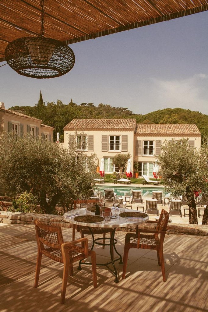 Elegant Mediterranean hotel exterior with terracotta walls, ivory shutters, and lush gardens framing a tranquil swimming pool in Saint-Tropez