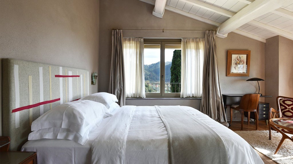 Elegant Tuscan-style hotel room with soft white linens, exposed wooden beams, terracotta floor, and panoramic countryside views through large windows