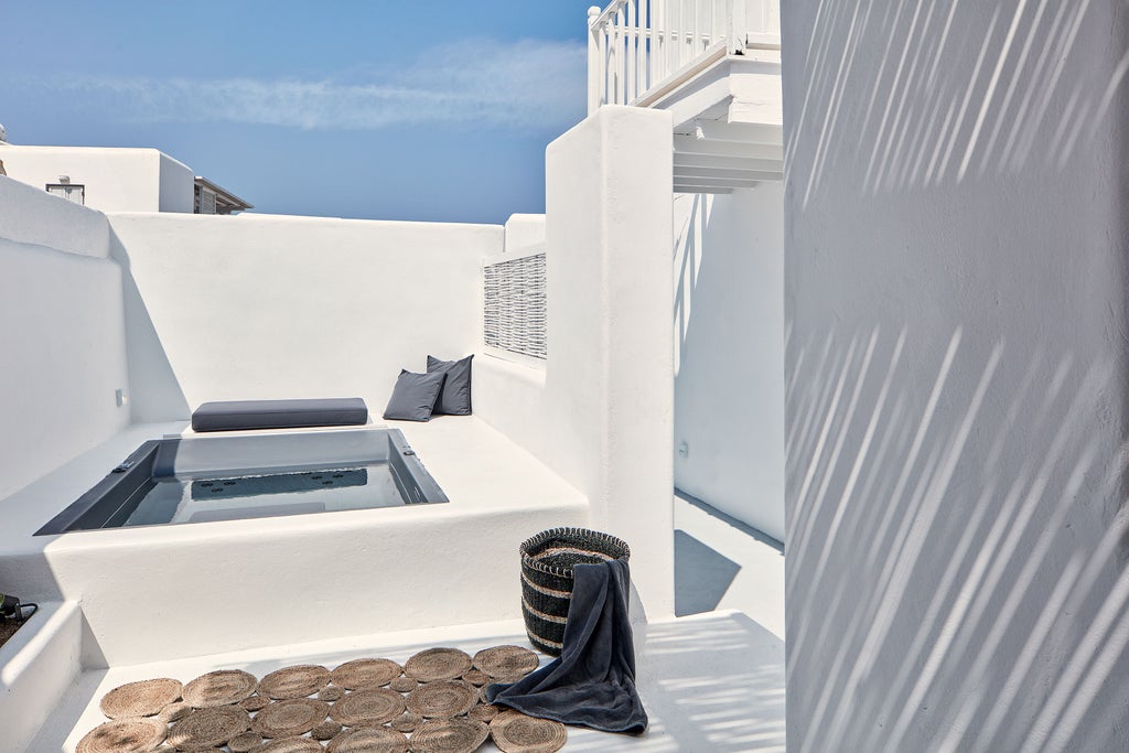 Luxurious white-washed suite with private infinity pool overlooking Santorini's caldera and Aegean Sea during golden sunset