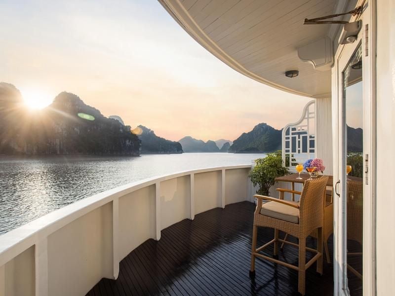 Luxurious Au Co Suite on Bhaya Cruises, featuring elegant wooden furnishings, plush bedding, and panoramic views of Halong Bay's scenic landscape