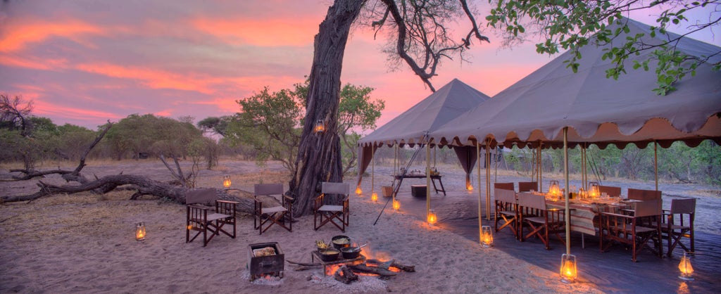 Luxury safari tent with wooden deck overlooking Savute landscape, canvas walls and elegant outdoor furnishings at sunset