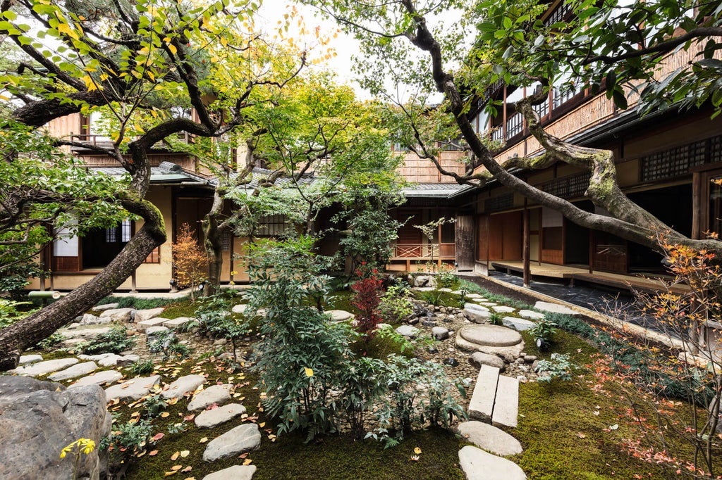 Traditional Japanese ryokan exterior with elegant stone pathway, bamboo fencing, and minimalist zen garden under warm lantern lighting at dusk