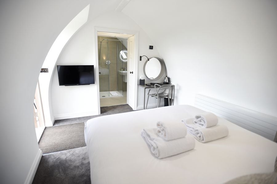 Serene luxury hotel room with soft neutral tones, plush bedding, rustic wooden furnishings, and large windows overlooking lush countryside at Tuddenham Mill