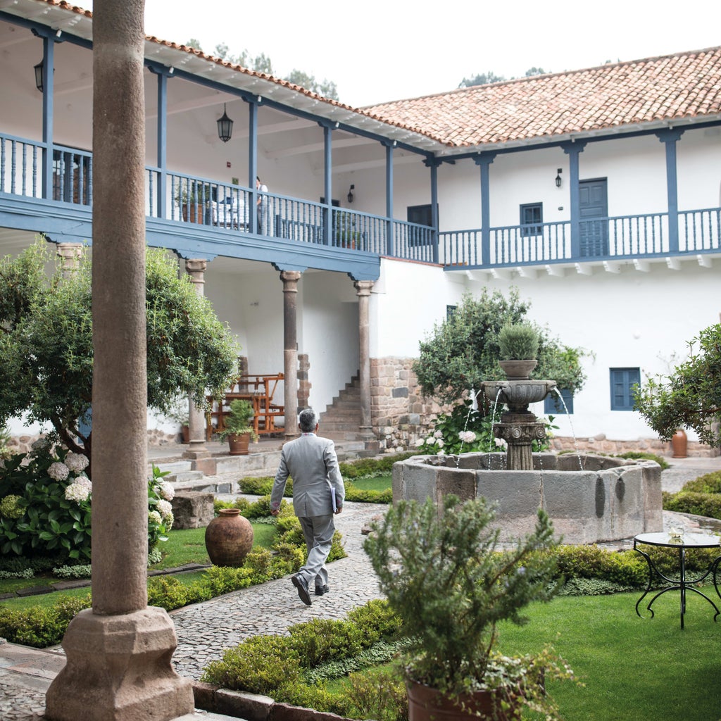 Historic luxury hotel in Cusco with stone archways, manicured courtyard gardens, and colonial-era architecture against Andean mountains