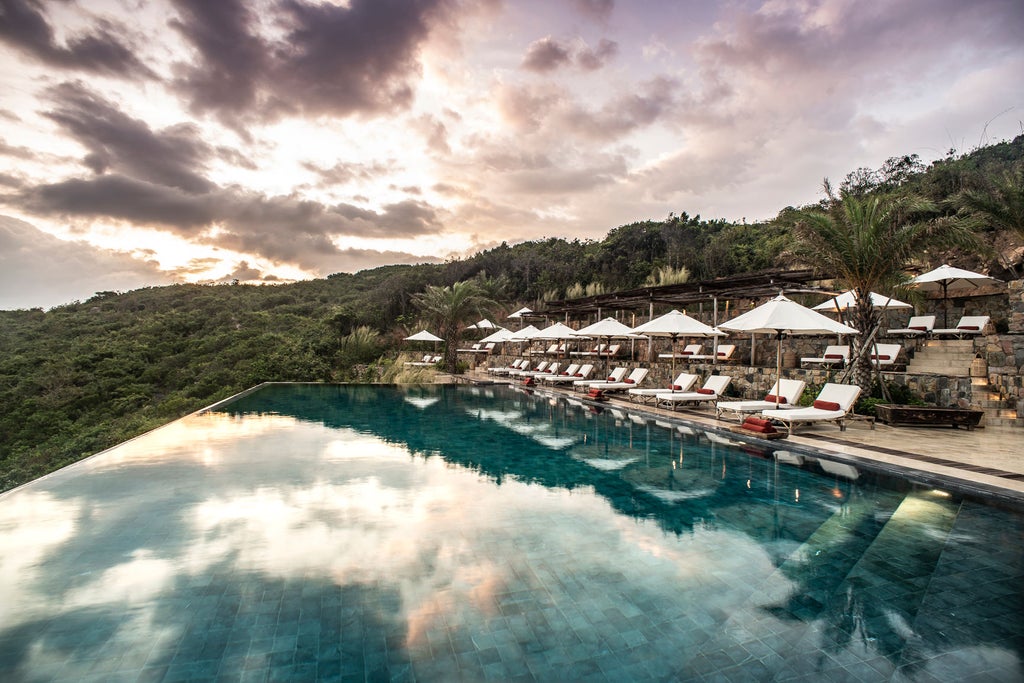 Serene infinity pool overlooking Vietnamese coastline at sunset, with traditional pavilions and lush tropical gardens at luxury resort