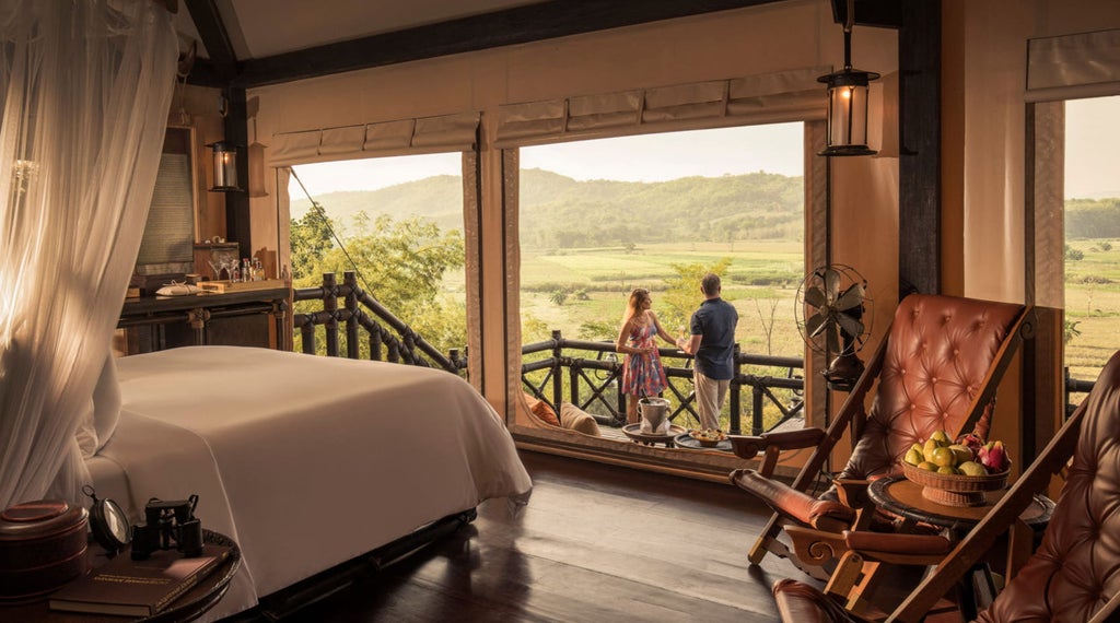 Luxurious safari-style tent suite with teak flooring, handcrafted furniture, canopy bed and outdoor deck overlooking Thai jungle