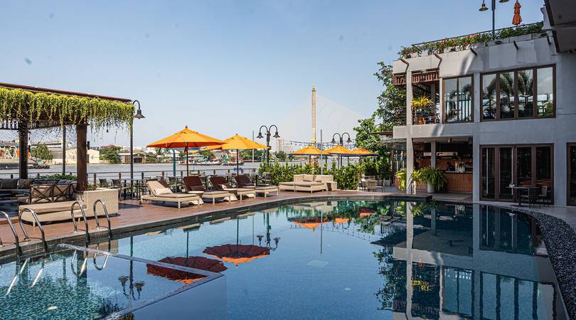 Elegant riverside hotel with infinity pool overlooking Bangkok's Chao Phraya River, featuring contemporary Thai architecture and lush gardens