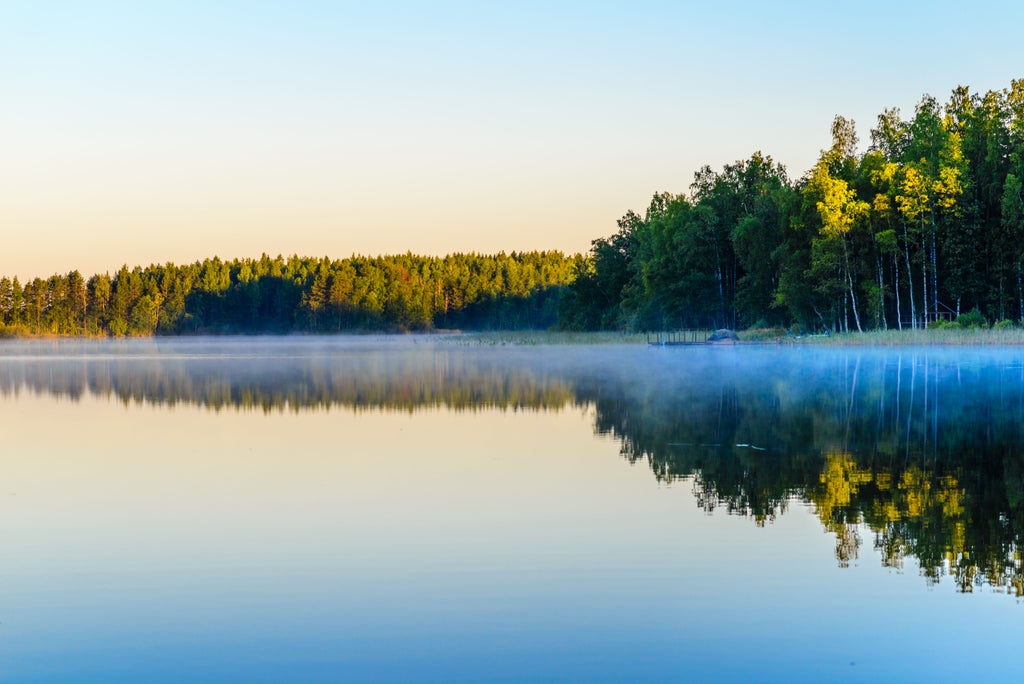 Serene sunset over Lake Saimaa, Finland's largest lake, with dense pine forests reflecting in crystal-clear waters and rocky islands