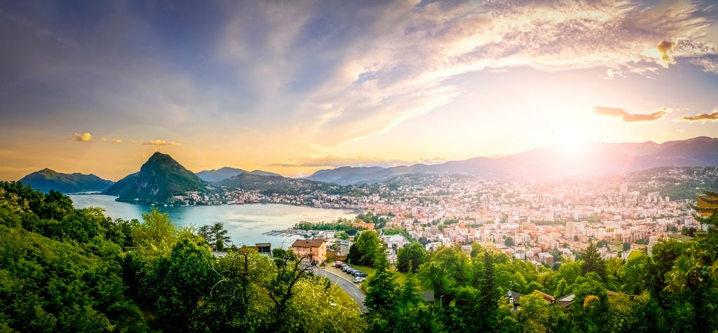 Luxury Lake Como waterfront villas nestled along steep cliffs, with snow-capped mountains reflected in calm turquoise waters at sunset