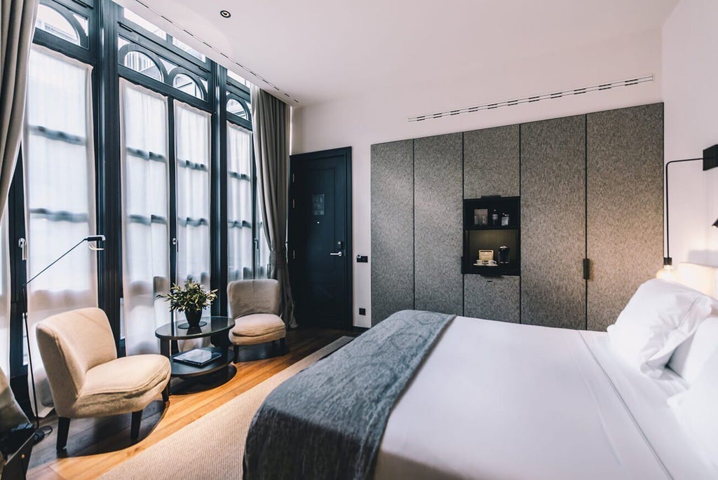 Elegant white-walled hotel room with minimalist design, high ceilings, modern wood furnishings, and large windows in historic Sant Francesc Hotel Singular, Mallorca