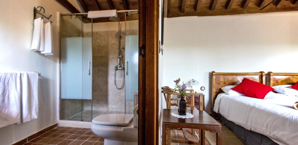 Elegant Spanish rural suite with rustic stone walls, antique wooden furniture, plush white bedding, and soft natural lighting in Cortijo del Marqués