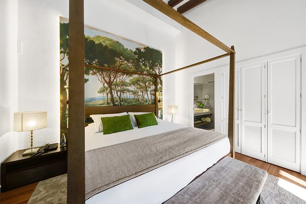 Elegant junior suite with blue-toned Mediterranean decor, plush king bed, modern wooden furniture, and panoramic window overlooking scenic landscape in Sóller, Spain