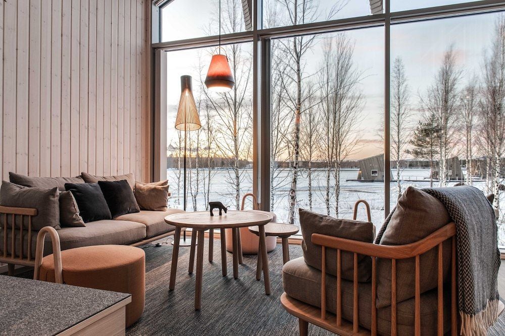 Minimalist wooden cabin suite with floor-to-ceiling windows overlooking frozen river, showcasing Scandinavian design and serene Arctic landscape at Arctic Bath hotel