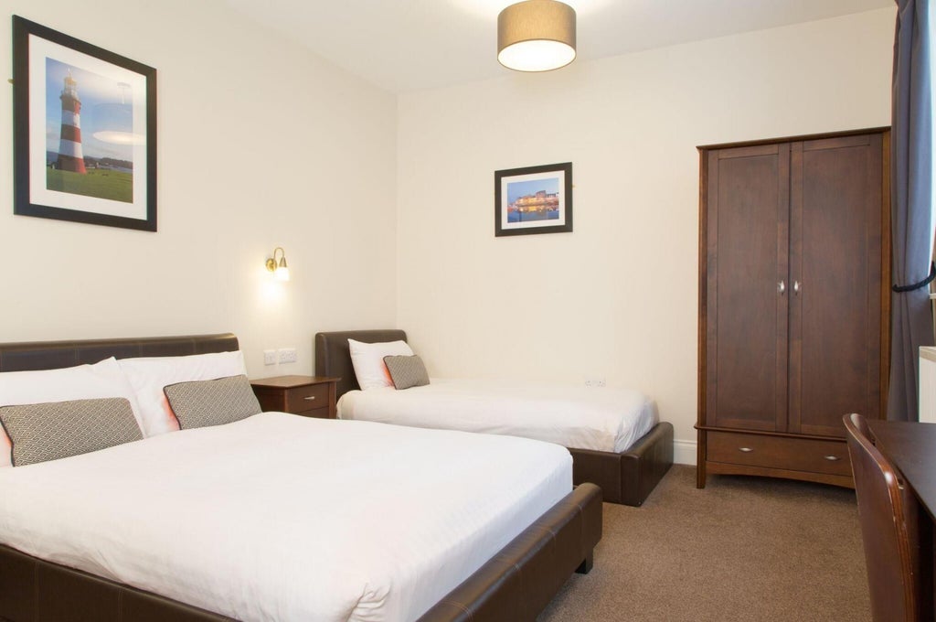 Twin room at The Scenset Plymouth hotel with two elegant beds, sophisticated neutral decor, soft lighting, and contemporary furnishings in a spacious layout.