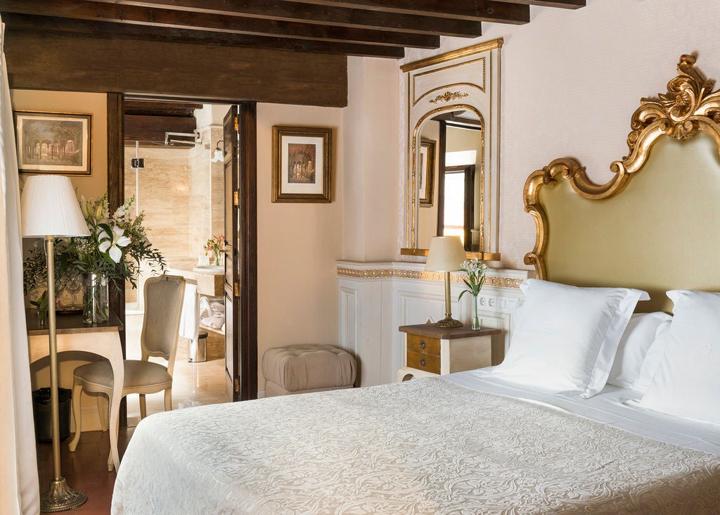 Elegant Spanish boutique hotel room with ornate chandelier, vintage-style furniture, draped curtains and exposed wood beam ceiling