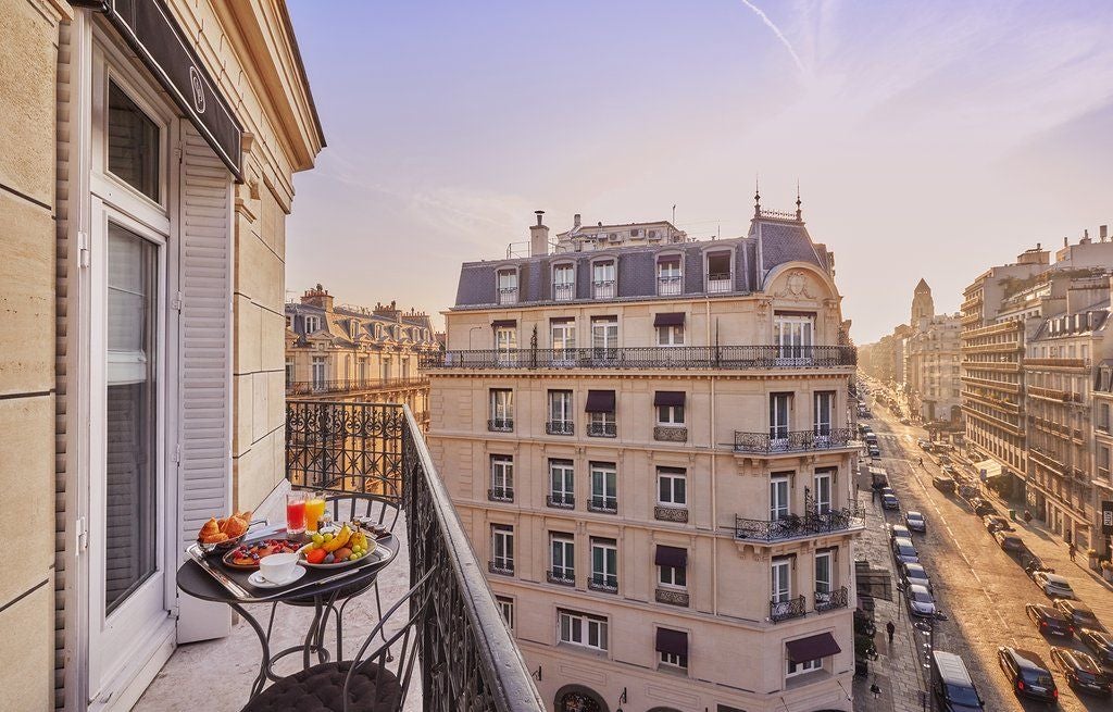 Elegant Parisian hotel facade with wrought-iron balconies, classic stone architecture, and French flags against a bright blue sky